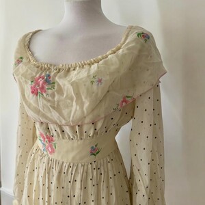 May include: A vintage cream-colored dress with a floral print and black polka dots. The dress has a ruffled neckline and long sleeves.
