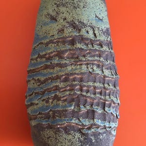 May include: A tall, green and brown ceramic vase with a textured surface. The vase has a wide mouth and a narrow base.