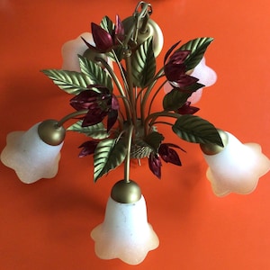 May include: A gold metal chandelier with five white glass shades shaped like bells. The chandelier is decorated with red and green metal flowers.