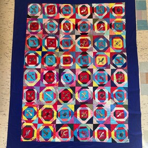 May include: A colourful quilt with a blue background and a repeating pattern of squares with embroidered lizards. The quilt is made of various fabrics in shades of red, pink, yellow, blue, green, and white.