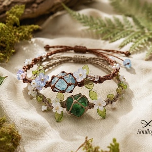 Puede incluir: Dos pulseras de macramé con piedras facetadas centrales en azul claro y verde oscuro, envueltas en redes de cordón marrón y beige. Las bandas están adornadas con pequeñas cuentas de flores blancas y azules y hojas verdes.