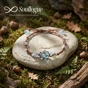 Puede incluir: Una pulsera trenzada marrón con detalles florales azules y blancos y un gran cristal azul. La pulsera se exhibe sobre una piedra gris rodeada de vegetación, bellotas y el texto "Soullogue Where love becomes timeless."