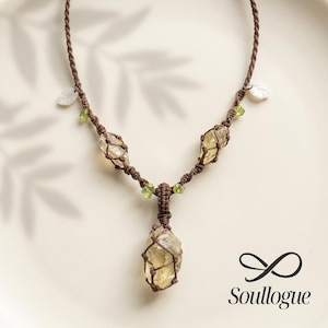 May include: A handcrafted necklace featuring three raw, light yellow citrine crystals encased in a brown macrame design. The necklace includes small green beads and white leaf accents. The pendant hangs from a brown cord.