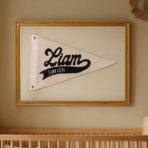 May include: A wooden crib with a white mattress and a white and black pennant hanging on the wall above it. The pennant says "Liam Smith".