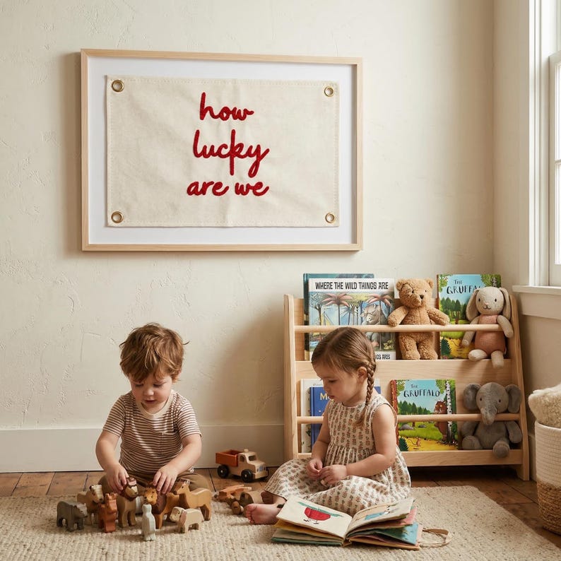 May include: A framed wall hanging with the text "how lucky are we" in red script. Two children are playing with wooden toys on a rug. A wooden bookshelf holds books and stuffed animals.