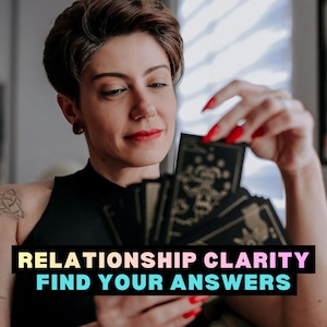 May include: A person holding a deck of tarot cards with the text "RELATIONSHIP CLARITY FIND YOUR ANSWERS". The cards have black backgrounds with gold illustrations. The person has red nail polish and lipstick.