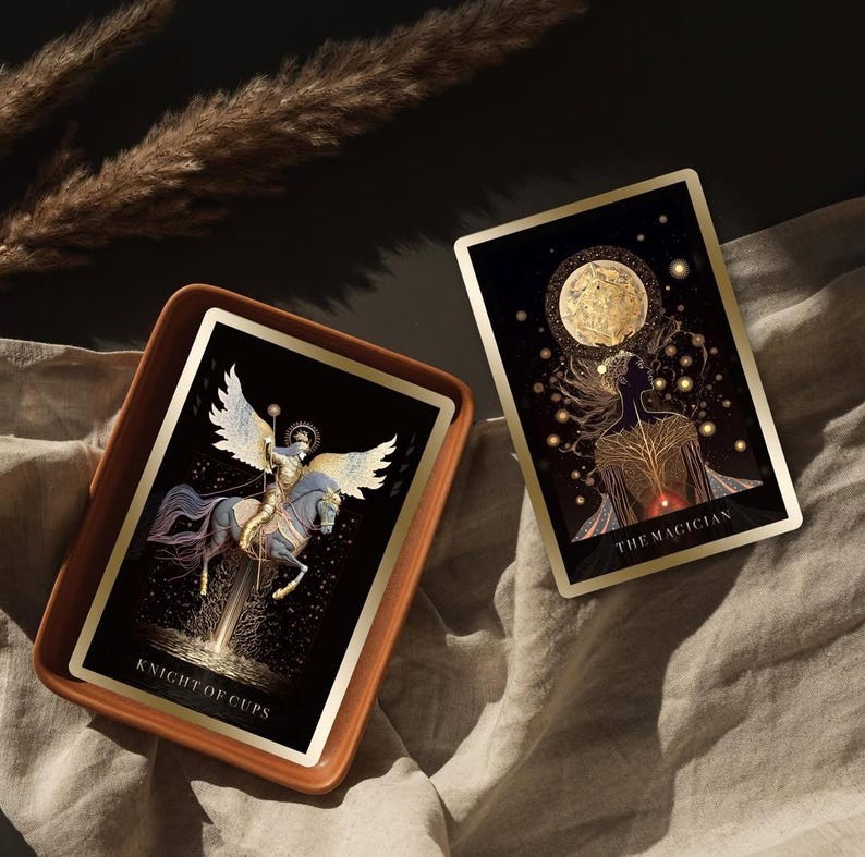 Pode incluir: Duas cartas de tar&ocirc; com detalhes dourados e fundos pretos s&atilde;o exibidas. Uma carta, rotulada "Knight of Cups", apresenta uma figura alada a cavalo. A outra carta, "The Magician", retrata uma silhueta com uma lua e estrelas.