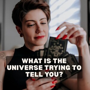 Puede incluir: Un mazo de cartas de tarot negras con ilustraciones de líneas doradas, sostenido por una persona con esmalte de uñas rojo. Las cartas muestran un bufón y el texto WHAT IS THE UNIVERSE TRYING TO TELL YOU? aparece en blanco sobre un fondo oscuro.