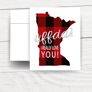 May include: A white card with a red and black plaid outline of the state of Minnesota. The text "uffda! I really love YOU!" is written in white on the card.