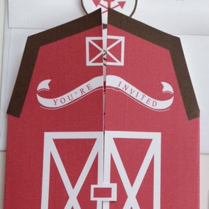 Puede incluir: Invitación en forma de granero rojo con una pancarta blanca que dice "You're Invited". El granero tiene un techo marrón y puertas blancas en forma de X.