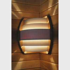 Puede incluir: Una lámpara de pared con un diseño en capas. La lámpara tiene un marco oscuro y presenta paneles horizontales y curvos que emiten un brillo cálido y acogedor. La luz está colocada contra una pared de madera.