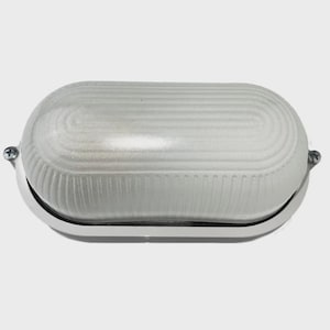 Puede incluir: Una lámpara de exterior blanca de forma ovalada con una cubierta de vidrio acanalado. La lámpara está montada sobre una base de metal plateado y asegurada con tornillos. El diseño es simple y funcional, adecuado para la iluminación exterior.