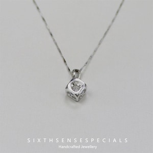 May include: A silver necklace with a cubic zirconia pendant in a cube shape.
