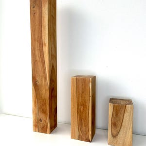 Op de afbeelding: Drie houten blokken van verschillende hoogtes en breedtes. De blokken zijn rechthoekig en gemaakt van lichtbruin hout met zichtbare nerfpatronen. De blokken zijn gerangschikt van hoog naar laag, waarbij de natuurlijke houttinten worden getoond.