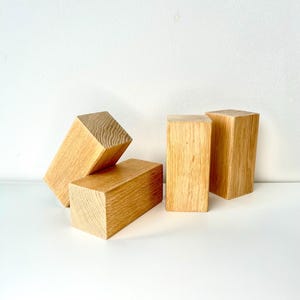 Op de afbeelding: Vier rechthoekige houten blokken met een natuurlijke houtnerf afwerking. De blokken zijn in een groep gerangschikt, met verschillende oriëntaties, tegen een witte achtergrond. Het hout heeft een lichtbruine kleur.
