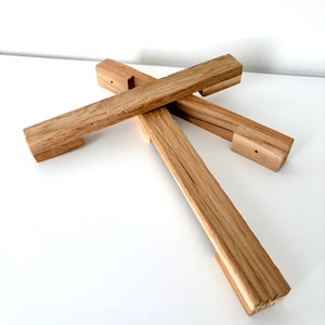 Könnte beinhalten: Vier Holz-Schrankgriffe aus hellbraunem Holz. Jeder rechteckige Griff hat eine kleine Kerbe und ein gebohrtes Loch. Die Griffe sind kreuzförmig auf einer weißen Oberfläche angeordnet.