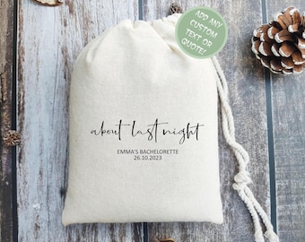 May include: A cream-colored drawstring bag with the text "about last night" in a handwritten font. Below the text is "EMMA'S BACHELORETTE 26.10.2023". A green circle with text is in the upper right corner. The bag is on a wooden surface.