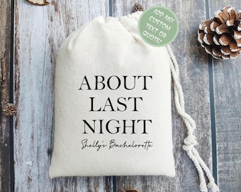 May include: A white drawstring bag with the text "ABOUT LAST NIGHT" and "Shelly's Bachelorette" printed on it. The bag is on a wooden surface.