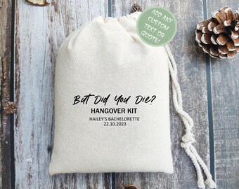 May include: A white drawstring bag with the text "But Did You Die? Hangover Kit" and the date "22.10.2023". The bag is on a wooden surface with a pine cone and other natural elements.