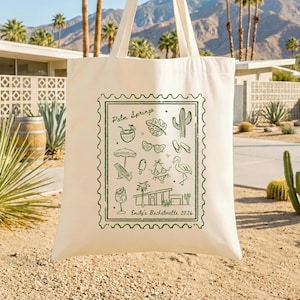 May include: Off-white tote bag with a green stamp-like design featuring Palm Springs illustrations. The design includes a cocktail, sunglasses, a cactus, and the text "Emily's Bachelorette 2026". The bag has two handles.