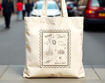 May include: A white canvas tote bag with a black and white illustration of New Orleans landmarks and the text "NOLA" and "Juliana's Bach".