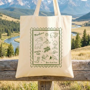 Può includere: Borsa tote color crema con un design verde a forma di timbro con illustrazioni a tema Montana. Il design include un sole, un orso, un bisonte e altre icone. Sono visibili anche i testi "Montana" e "Your text here".