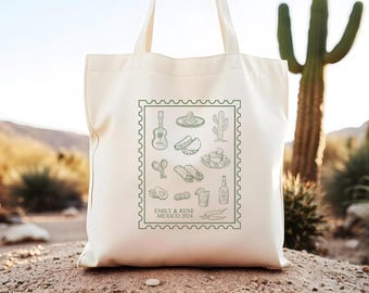 Puede incluir: Una bolsa de lona blanca con un diseño de sello verde que presenta varias ilustraciones de temática mexicana, incluyendo una guitarra, un sombrero, tacos y tequila. El texto "Emily & Rene Mexico 2024" está impreso debajo del sello.