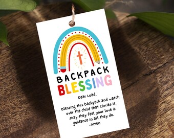May include: A rectangular white gift tag featuring a colorful rainbow graphic shaped like a pencil, a small orange cross, and the text BACKPACK BLESSING. Below, a prayer is printed: Dear Load, blessing this backpack and watch over the child.