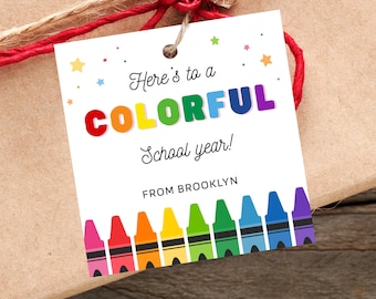 May include: A square white gift tag with a hole at the top, featuring the text Here's to a COLORFUL School year! and FROM BROOKLYN. The design includes colorful stars and a row of multi-colored crayons at the bottom, attached with red twine.