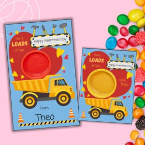 May include: Two Valentine's Day cards featuring a yellow dump truck with a red heart and the text "You're Loads of Fun!" and "Happy Valentine's Day". The cards are blue with yellow construction cones and a small container for play dough.