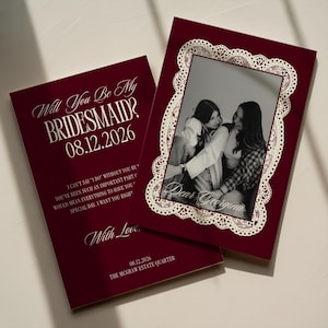 May include: Two deep burgundy cards featuring white text and a black-and-white photograph. One card reads Will You Be My BRIDESMAID? 08.12.2026. The other card displays a photo framed by a white lace border with the text Dear Georgina written below.