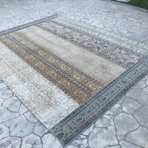 May include: Rectangular area rug with a distressed, vintage look. The rug features a central beige stripe flanked by patterned borders in cream, brown, and blue. The rug's edges are trimmed with a blue border.