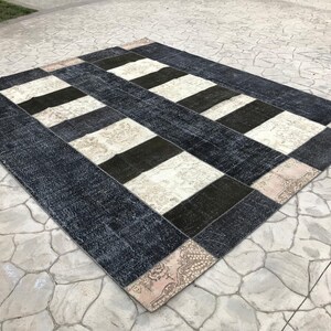 May include: A rectangular patchwork rug with a geometric design. The rug features alternating stripes of dark blue, black, and cream colors. The rug has a distressed, vintage appearance, with a faded look.