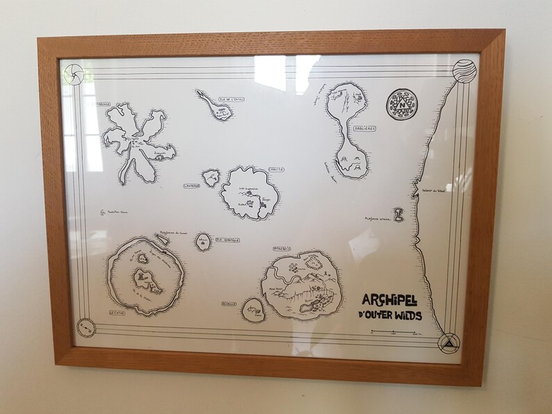 May include: A framed black and white map titled 'Archipel d'Outer Wilds' with various islands and names of locations. The map is on a white background and is framed in a light brown wood frame.