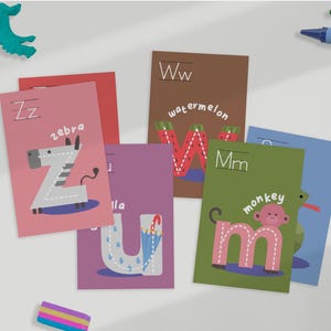 Op de afbeelding: Kleurrijke flashcards met letters van het alfabet en bijbehorende illustraties van dieren of objecten. De kaarten tonen de letters Zz voor zebra, Ww voor watermeloen, Mm voor aap en Uu voor paraplu.