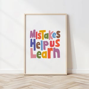 May include: A framed print featuring the phrase "Mistakes Help Us Learn" in vibrant, multi-coloured lettering. The words are set against a white backdrop, with a light-toned wooden frame. The colours include purple, orange, green, and blue.