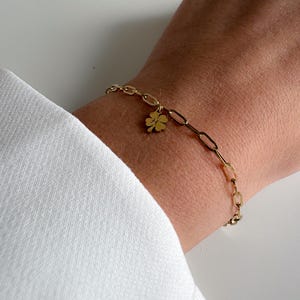 Könnte beinhalten: Ein goldenes Kettenarmband mit einem vierblättrigen Kleeblatt-Anhänger.