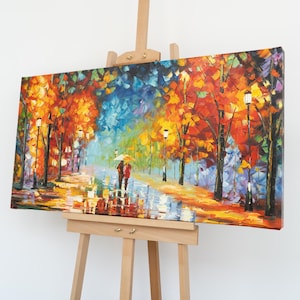 Puede incluir: Pintura al óleo sobre lienzo que representa una vibrante escena otoñal. Una pareja camina bajo un paraguas por un camino mojado, bordeado de árboles en tonos rojos, naranjas y amarillos. Las farolas iluminan la escena, creando un ambiente cálido.