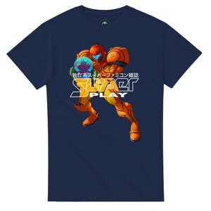 May include: A navy blue short-sleeve t-shirt featuring a graphic of a character in orange and yellow armour holding a glowing blue orb. The text "独立系スーパーファミコン雑誌" and "SUPER PLAY" are printed in white and yellow over the character.
