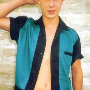 May include: A young person wearing a teal and black bowling shirt with the collar open. The shirt has a button closure and a pocket on the left side.