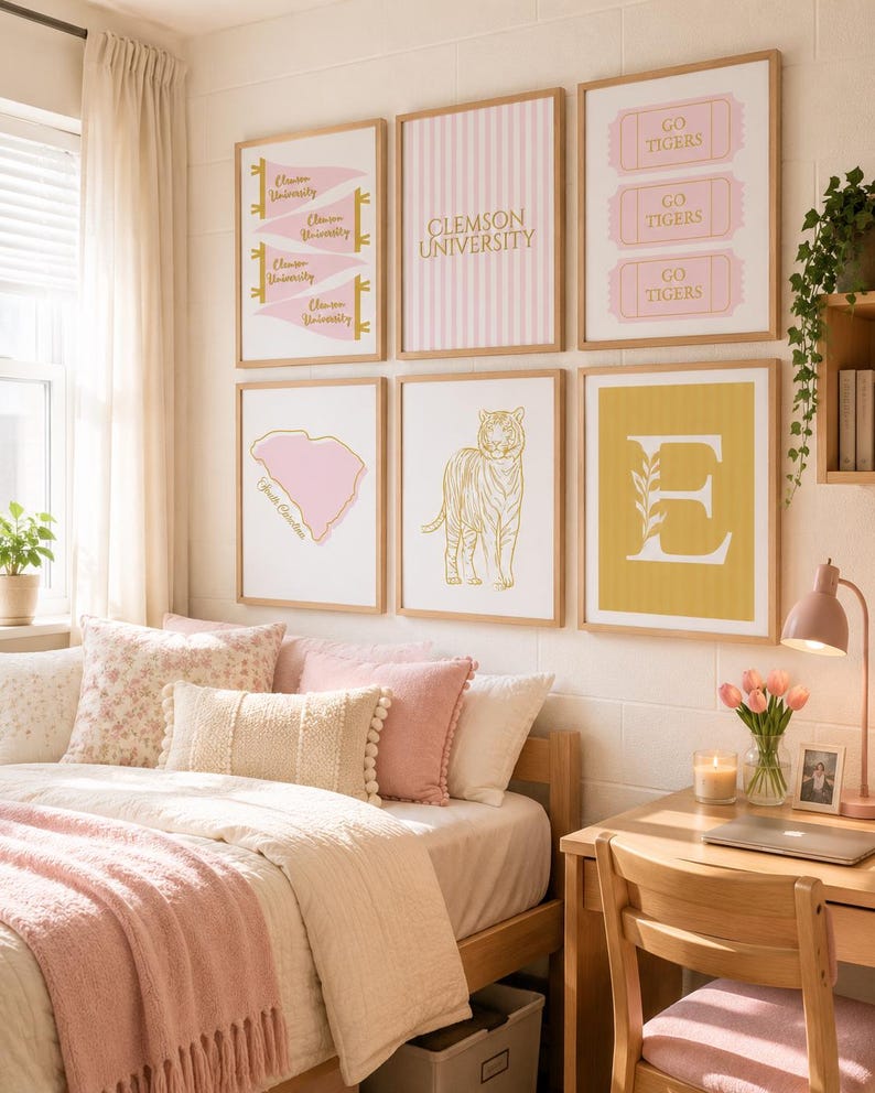 May include: A gallery wall of six framed prints featuring Clemson University themes, including pink pennants, striped backgrounds, ticket stubs with Go Tigers text, a South Carolina map, a gold tiger illustration, and a large letter E on yellow.