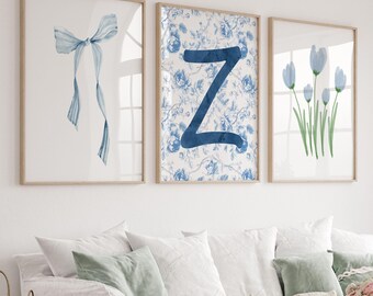 May include: Three framed wall art prints. The first features a watercolor bow in shades of blue. The second displays a blue floral pattern with a large blue letter "Z". The third print shows blue flower stems. All are in light wood frames.