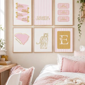 May include: A set of six framed wall art prints featuring Clemson University themes in pink, white, and gold. Designs include pennants, striped patterns, ticket stubs with Go Tigers text, a South Carolina map, a tiger illustration, and a letter E.