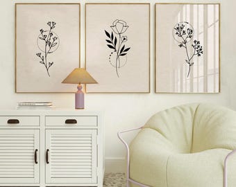 Puede incluir: Tres impresiones minimalistas de arte lineal con diseños florales y círculos. Las impresiones están enmarcadas en oro y colgadas en una pared blanca sobre un armario blanco y un sillón verde claro.
