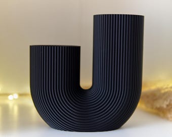 Puede incluir: Un jarrón de cerámica negro con un diseño único en forma de U. El jarrón tiene una textura acanalada y es perfecto para exhibir flores u otros artículos decorativos.