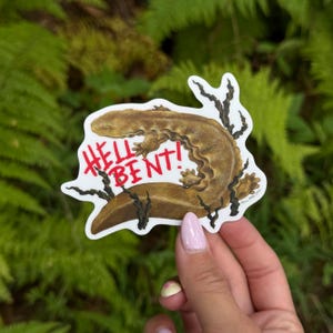 May include: A die-cut sticker featuring a brown, textured salamander illustration with dark, spindly root-like accents. The text HELL BENT! is printed in bold, distressed red lettering across the centre of the salamander's body on a white background.