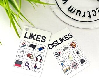 May include: Two white rectangular cards with the words "LIKES" and "DISLIKES" in black. Each card has illustrated icons representing various interests and aversions. The "LIKES" card shows a pencil, a game controller, a candy bar, a music note, bread, headphones, a stage, a magnifying glass, and a soccer player.
