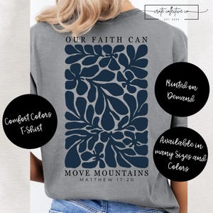 Puede incluir: Una camiseta gris Comfort Colors con un diseño floral azul marino y el texto "OUR FAITH CAN MOVE MOUNTAINS" de Mateo 17:20. La camiseta también tiene el texto "Printed on Demand" y "Available in many Sizes and Colors".