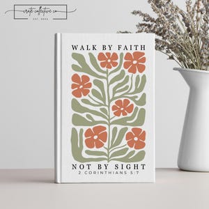 Puede incluir: Un libro blanco con el texto "WALK BY FAITH NOT BY SIGHT 2 CORINTHIANS 5:7" y un diseño floral en naranja y verde. El libro está de pie. La esquina superior izquierda tiene el texto "crate collective co EST. 2024".