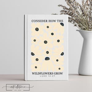 Puede incluir: Un diario de tapa dura blanco con el texto "CONSIDER HOW THE WILDFLOWERS GROW" y "LUKE 12:27". La portada presenta un diseño floral con flores color crema y centros azul marino. Un jarrón blanco con lavanda seca está en el fondo.